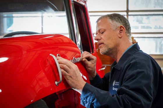 A person putting an emblem on a red truck.